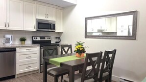 Une cuisine compacte avec des meubles blancs, un four à micro-ondes, une cuisinière et un lave-vaisselle. On y trouve une table à manger avec des chaises et une plante en pot posée sur la table.