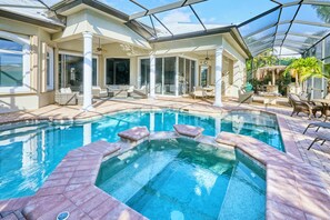 Ein Schwimmbecken mit Whirlpool, umgeben von Gartenmöbeln und überdachten Sitzbereichen.