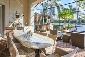 Eine sonnige Terrasse mit Esstisch, Stühlen und Grillbereich mit Blick auf ein Gewässer.