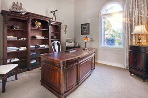 Ein Arbeitszimmer mit großem Holztisch, Bücherregal, Globus, Teleskop und einem Fenster mit Blick ins Grüne.