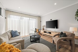 A modern living room with a sofa, armchair, coffee table, and a flat-screen TV mounted on the wall. - The Salty Snapper (Rhyll)