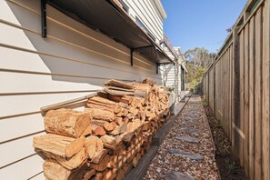 A stack of firewood against a white building with horizontal siding. - The Salty Snapper (Rhyll)