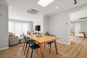 Ein modernes Wohnzimmer mit Essbereich, einem flachbildfernseher an der Wand und einem großen Fenster mit Vorhängen.