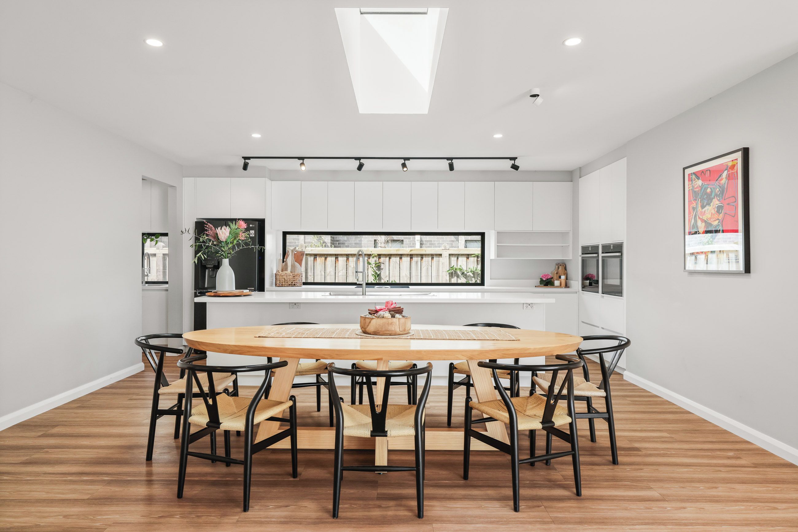 A modern kitchen with white cabinets, a central island, and a dining area with a round table and chairs.