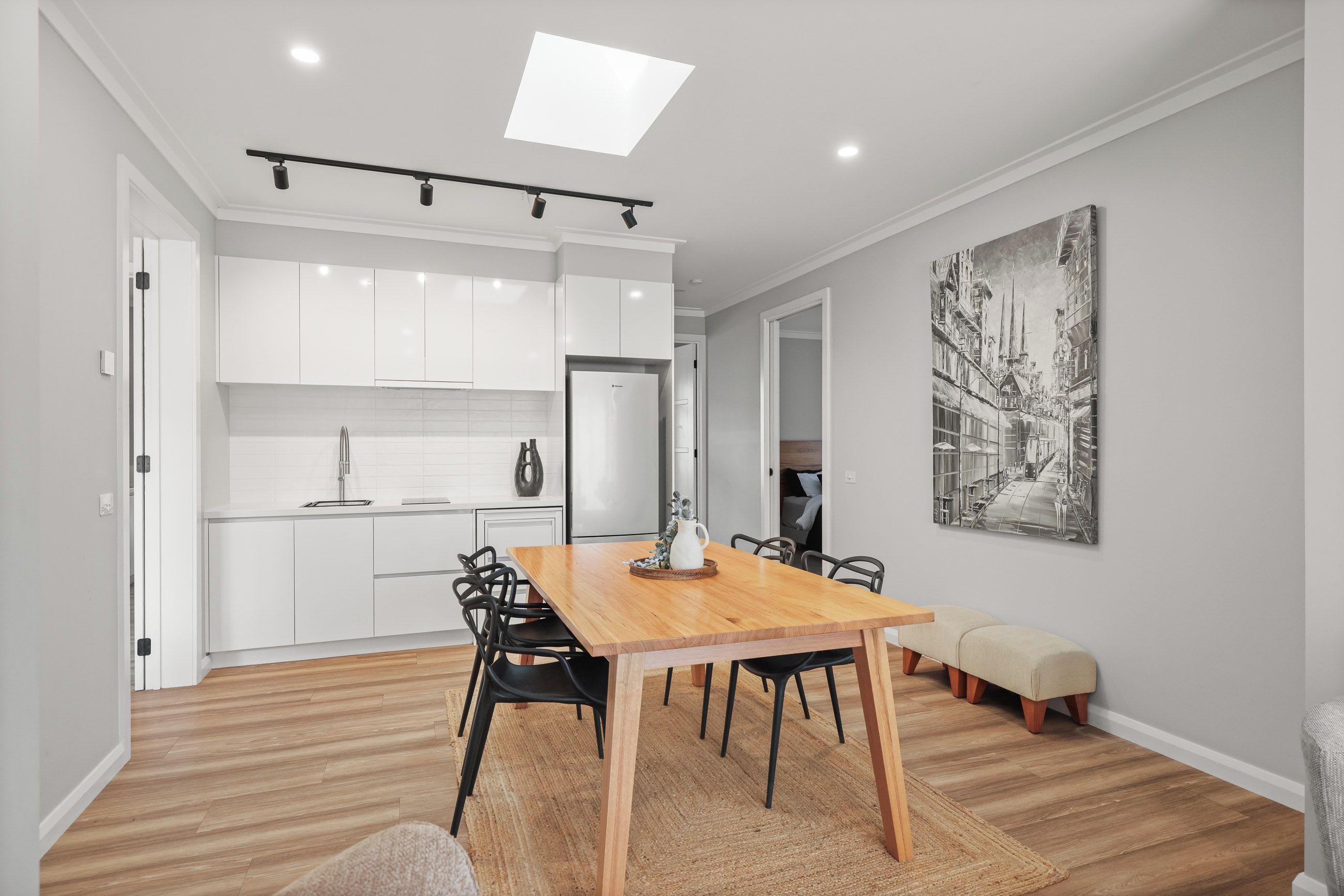 Une cuisine moderne avec des meubles blancs, un îlot central et un coin repas comprenant une table et des chaises en bois.