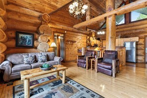 A log cabin interior with a sofa, leather chairs, a dining table, and a kitchen area. - Hot Tub + Arcade + Billiards | Mountain Views + Outdoor Dining | Bear Paw Cabin (Gatlinburg)