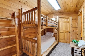 A wooden cabin with a bunk bed, a door, and a small table with towels. - Hot Tub + Arcade + Billiards | Mountain Views + Outdoor Dining | Bear Paw Cabin (Gatlinburg)