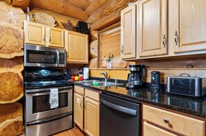 A kitchen with wooden cabinets, stainless steel appliances, and a granite countertop. - Hot Tub + Arcade + Billiards | Mountain Views + Outdoor Dining | Bear Paw Cabin (Gatlinburg)