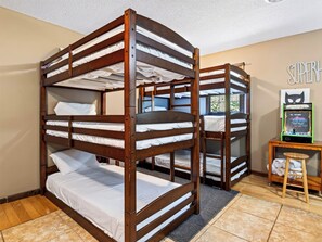 A bunk bed room with a small table and a poster on the wall. - Cathedral Ceilings + Hot Tub + Game Room | Fairway Views | Creek & Green (Gatlinburg)