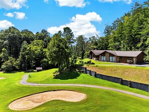 A golf course with a house on a hill, surrounded by trees. - Cathedral Ceilings + Hot Tub + Game Room | Fairway Views | Creek & Green (Gatlinburg)