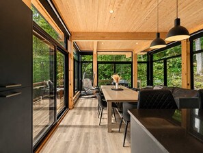 A modern interior with a wooden ceiling, large windows, and a dining area with chairs and a table. - Hot Tub | Forest | 10 Guests | Whiskey Mountain (Nominingue)