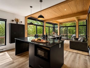 A modern kitchen with a central island, large windows, and a wooden ceiling. - Hot Tub | Forest | 10 Guests | Whiskey Mountain (Nominingue)