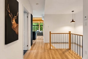 A hallway with wooden flooring, a staircase with a wooden railing, and a painting of a deer on the wall. - Hot Tub | Forest | 10 Guests | Whiskey Mountain (Nominingue)