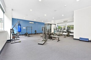 Un gimnasio con diversos equipos de ejercicio, un saco de boxeo y una banca.