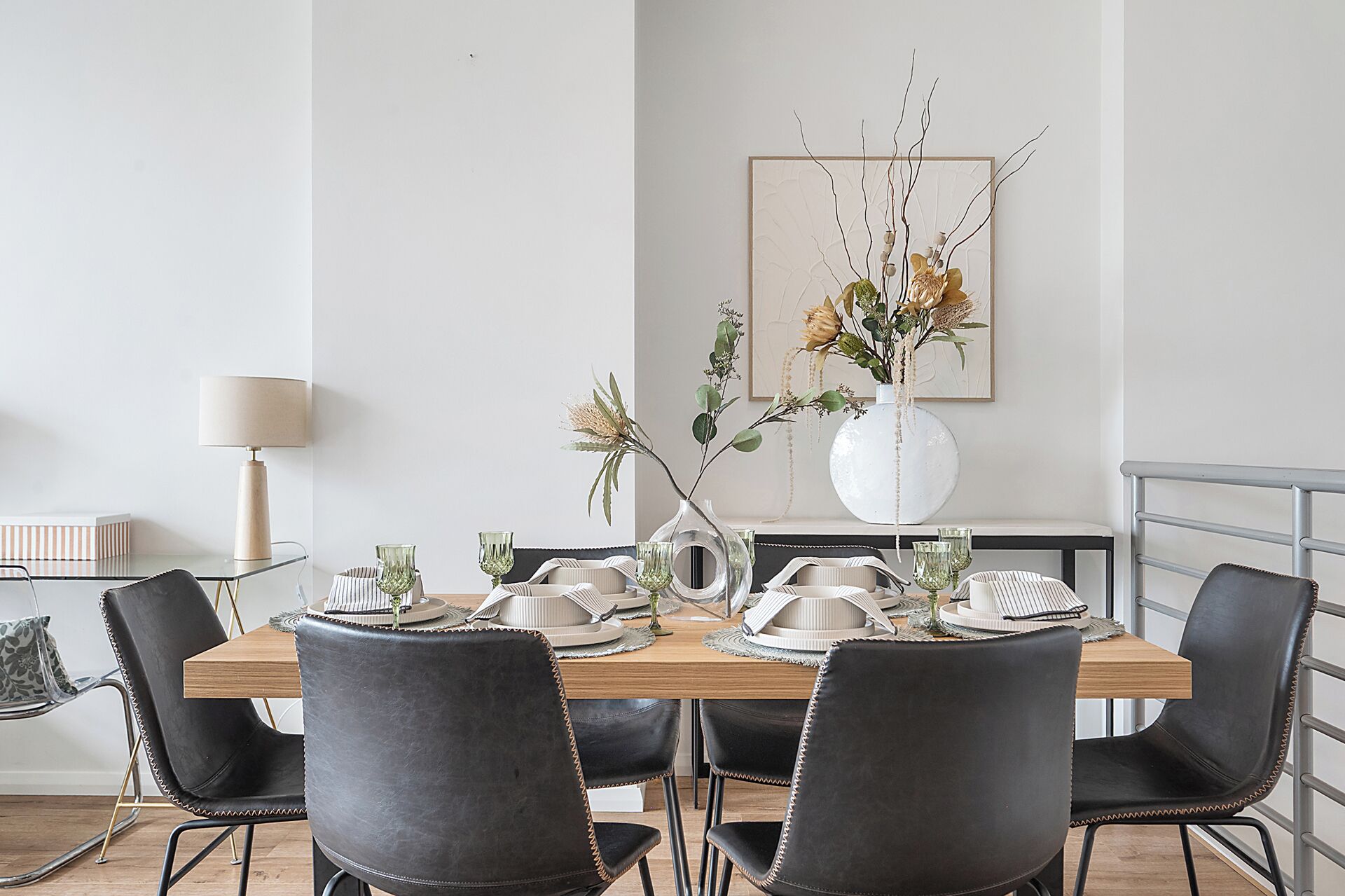 Comedor con mesa de madera dispuesta para cuatro, rodeada de sillas negras con detalles dorados.