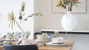 A dining table set with plates, glasses, and a vase with dried flowers. - Mascot Luxe 2BR | Airport | Pool + 2 Parking (Mascot)
