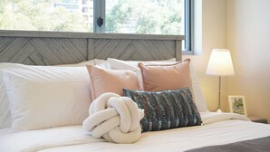 A bed with white linens, a decorative pillow, a fluffy white throw, and a bedside lamp. - Mascot Luxe 2BR | Airport | Pool + 2 Parking (Mascot)