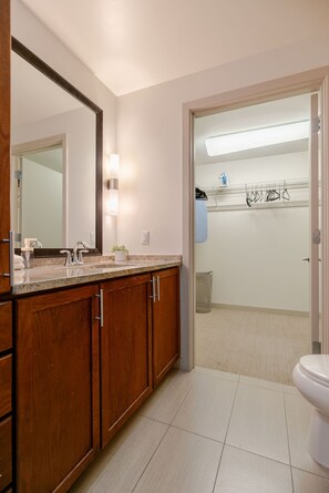 A bathroom with a wooden vanity, a large mirror, a sink, and a toilet. - Dallas Suite I Luxury High Rise (Dallas)
