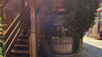 A rustic wooden staircase leading to a covered area with a brick wall and a wooden barrel.