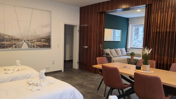 A hotel room with two beds, a dining table with chairs, a painting on the wall, and a view of the outdoors through a window. - Stylish and central apt 5 guests 65qm top location (Hanover)