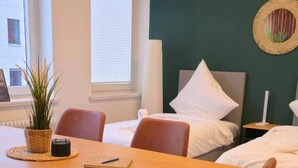 A hotel room with a bed, a dining table with chairs, a potted plant, and a window. - Stylish and central apt 5 guests 65qm top location (Hanover)