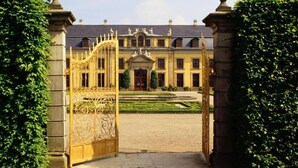 A grand entrance with a wrought iron gate leading to a classical building with a symmetrical facade and a manicured garden. - Stylish and central apt 5 guests 65qm top location (Hanover)