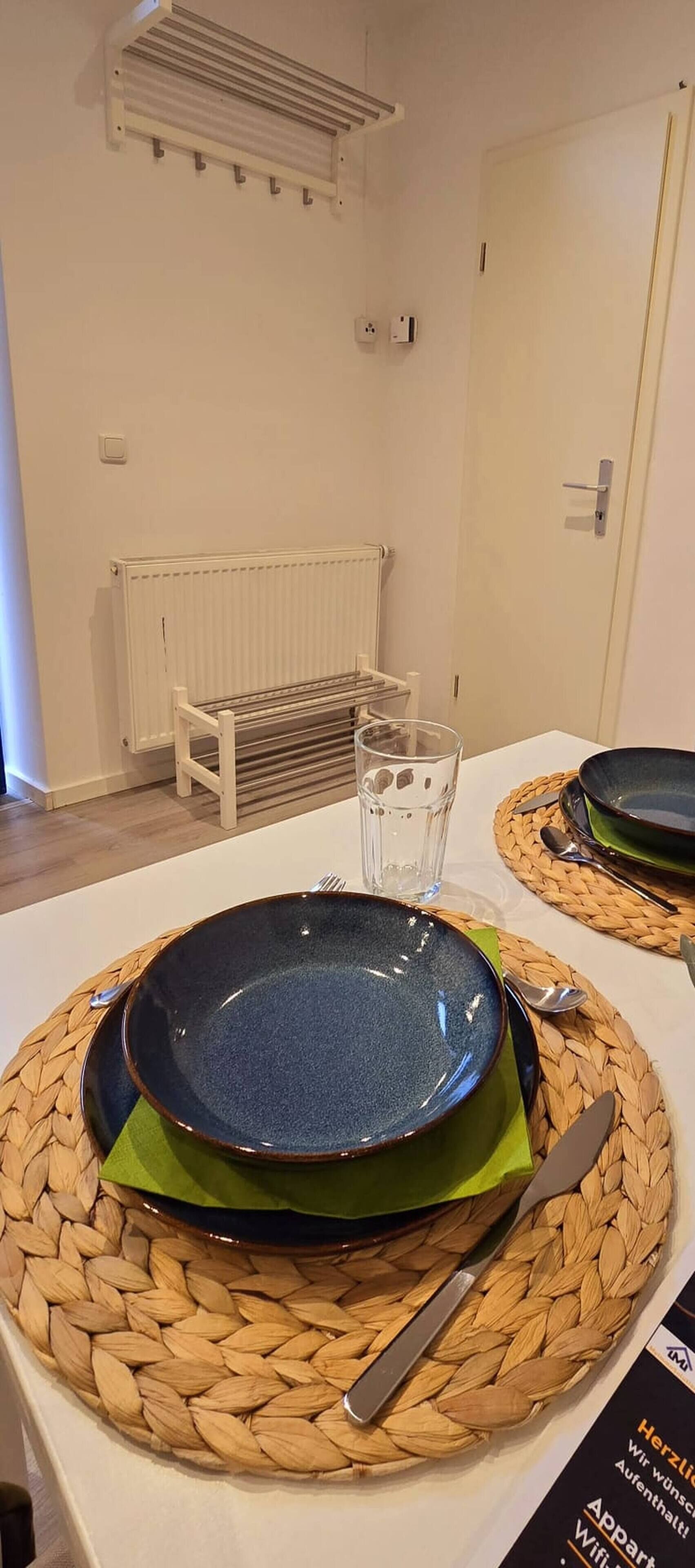 A table set with a plate, glass, and cutlery, a radiator, and a door in a room.