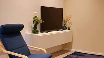 Una sala de estar moderna con un sillón azul, un televisor sobre un mueble blanco y una planta decorativa.