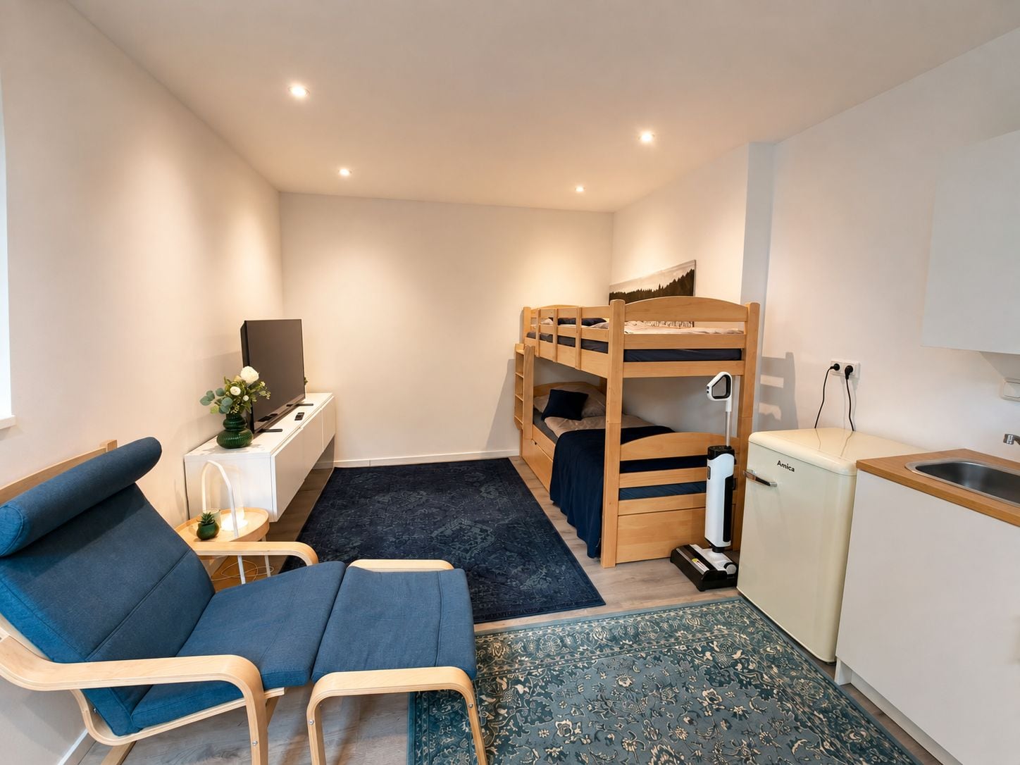 A compact room with bunk beds, a desk with a computer, a chair, and a small kitchenette.