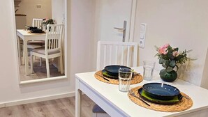 Un coin repas avec une table blanche, deux chaises et un vase rempli de fleurs.
