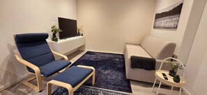 A modern living room with a blue armchair, a beige sofa, a small side table, a flat-screen TV, and a framed picture on the wall. - Mutterstadt Oasis Two Apartment (Mutterstadt)