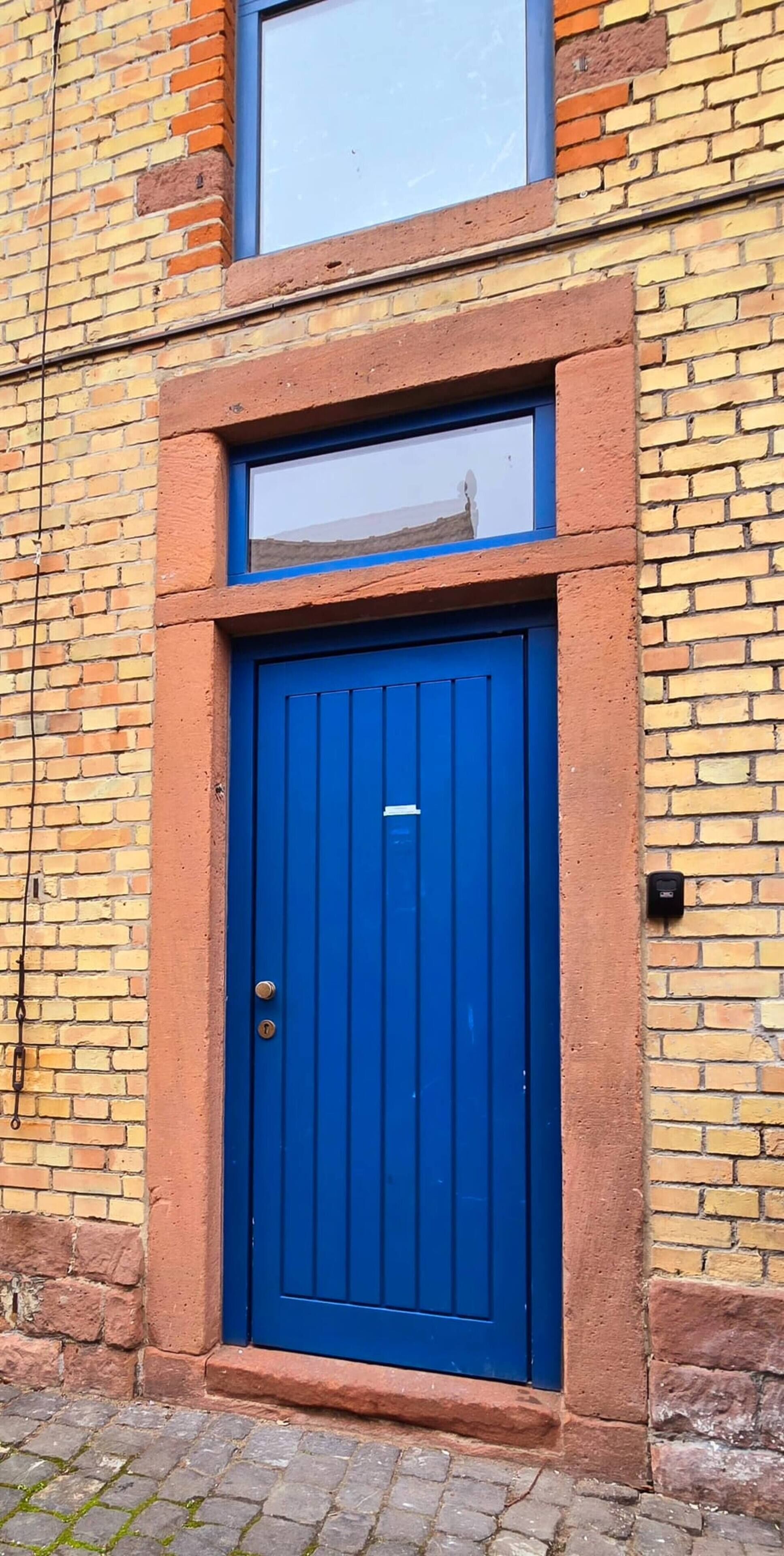 A blue door with a window above it, set in a brick wall.