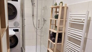 Une petite salle de bain comprenant une douche, des toilettes et un lave-linge.