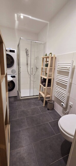 A compact bathroom with a shower, toilet, and washing machine. - Mutterstadt Oasis Two Apartment (Mutterstadt)