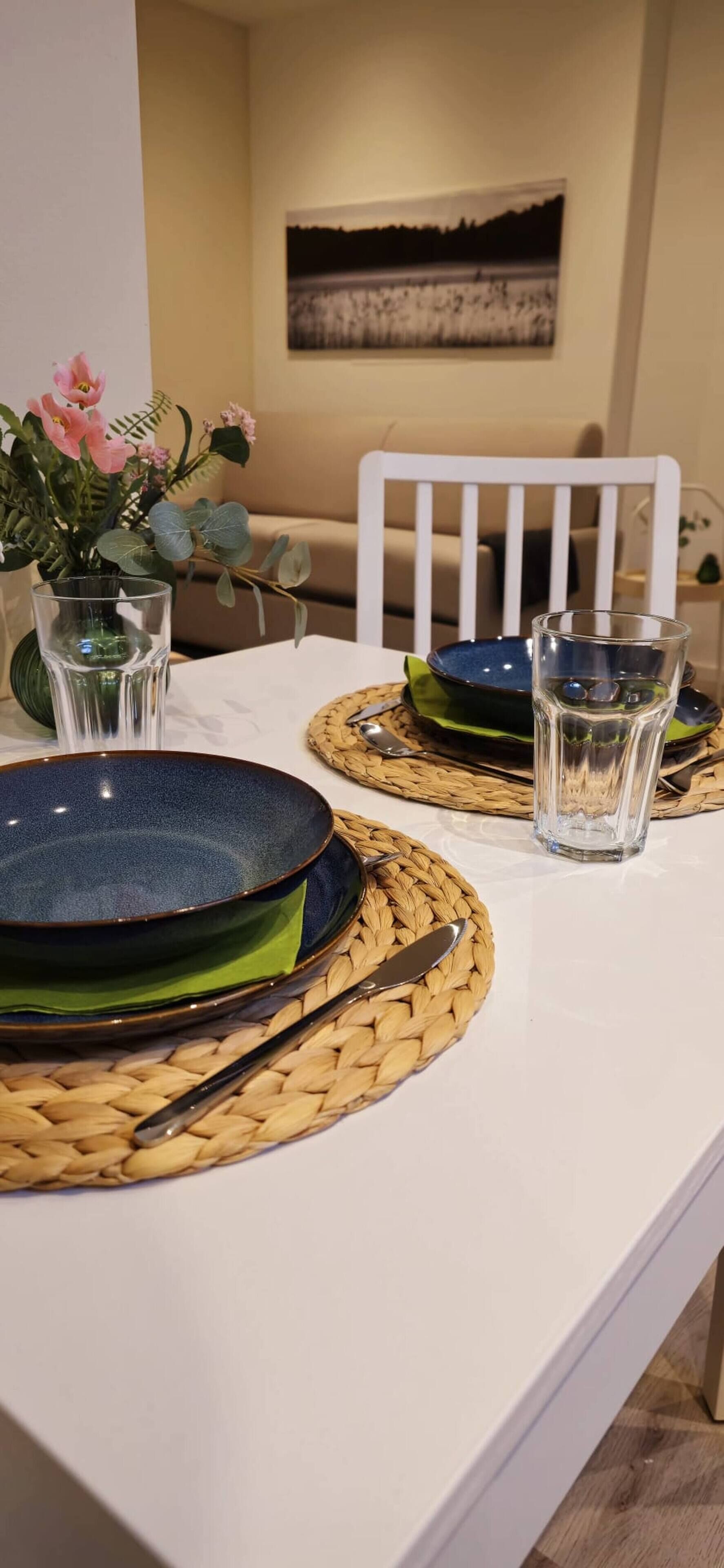 A dining table set with plates, bowls, and cutlery, with a vase of flowers and a painting on the wall.