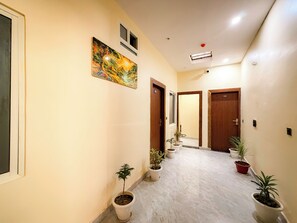 A hallway with potted plants, a painting, and doors numbered 104 and 106. - Hotel Avyan Palace (Vrindavan)