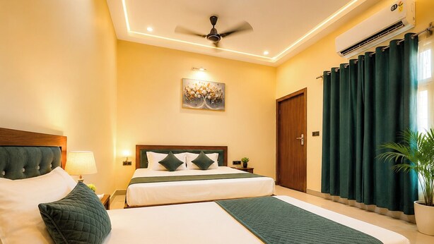 Quarto de hotel com duas camas, ventoinha no teto, aparelho de ar condicionado, um quadro na parede e uma planta em vaso.