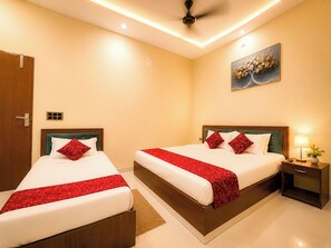 A hotel room with two beds, a ceiling fan, a nightstand with a lamp, and a painting on the wall. - Hotel Avyan Palace (Vrindavan)