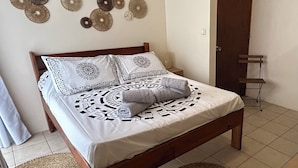 Ein Bett mit gemusterten Betttextilien, einem gewebten Teppich und Wandbildern.