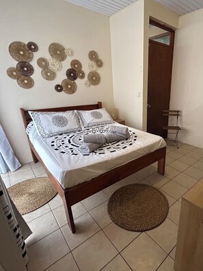 A bed with patterned bedding, a woven rug, and decorative wall art. - Vaihina Room (Raiatea)