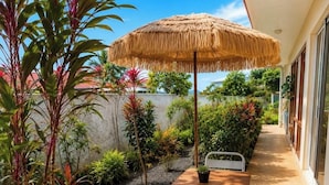 Eine Terrasses mit Tisch, Stühlen, einem Reetdachschirm und verschiedenen Pflanzen.