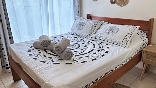 Ein ordentlich bezogenes Bett mit gemustertem Überwurf und Kissen, ein Holz-Kopfstück und eine Wand mit dekorativer Wandkunst.