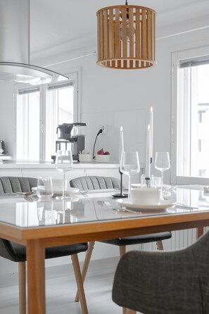 A modern dining area with a glass table, wooden chairs, and a hanging light fixture. - Taiga Penthouse, Private Sauna By Lapland Host (Rovaniemi)