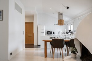 Une cuisine moderne avec des appareils électroménagers blancs, un coin repas avec une table et des chaises en bois, et un luminaire suspendu.