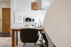 Une cuisine moderne avec des meubles blancs, une table à manger en bois et une chaise à l’assise rembourrée de couleur foncée.