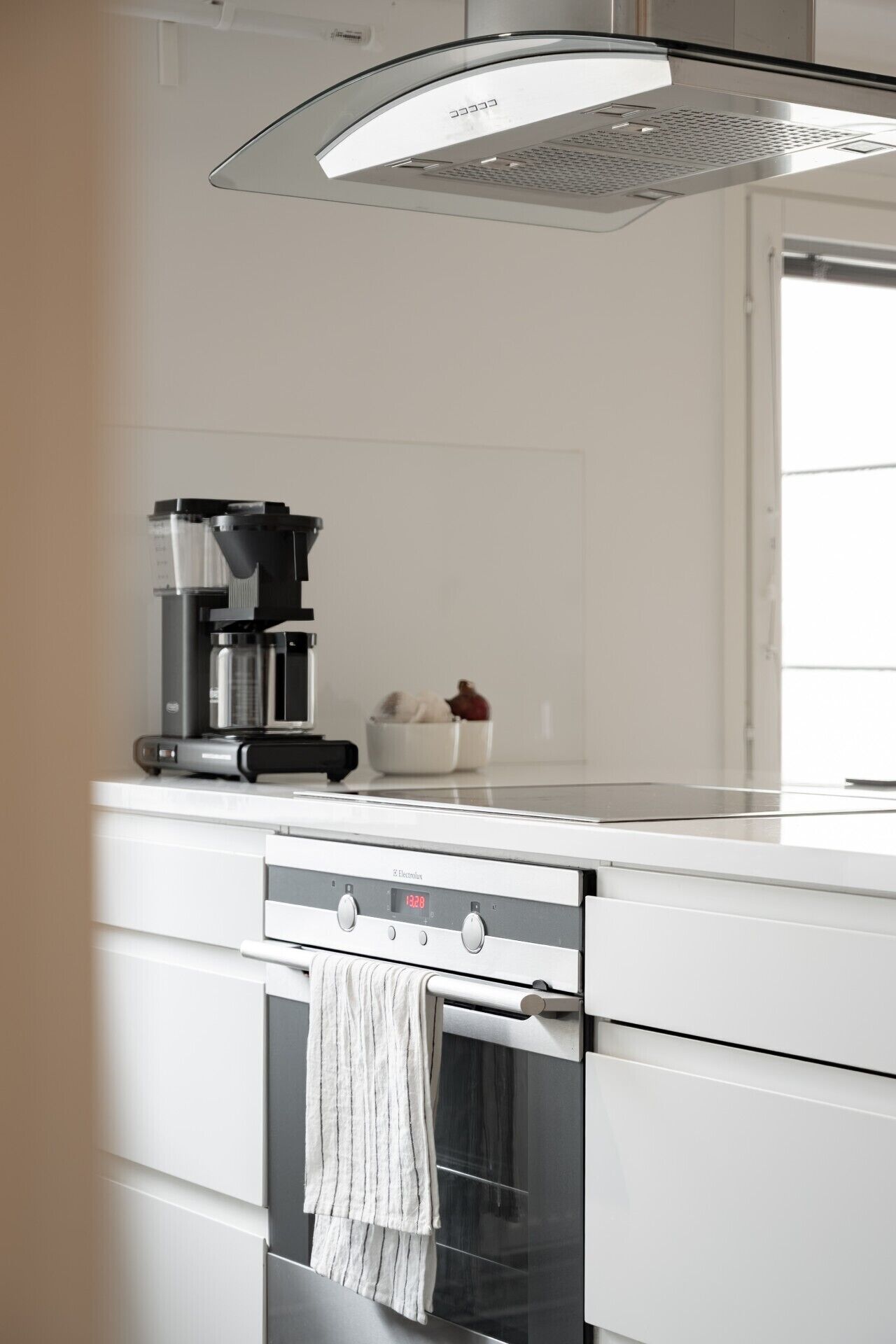 Eine moderne Küche mit Kaffeemaschine, Obstschale und digitaler Uhr, die 12:28 anzeigt.