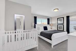 A bedroom with a white crib, a bed with a dark headboard, a window with blinds, and a ceiling light. - Private Heated Pool + Themed Rooms | Storey Lake (Kissimmee)