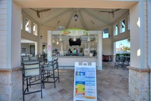 A covered outdoor seating area with tables and chairs, a central counter, and a menu board. - Private Heated Pool + Themed Rooms | Storey Lake (Kissimmee)