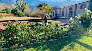 Ein Garten mit einer Fontäne, ein Gebäude mit Rundbogenfenstern und Berge im Hintergrund.