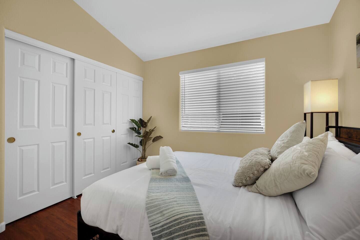 Une chambre à coucher avec un lit, des rideaux blancs, une fenêtre, une lampe de chevet et une plante en pot.